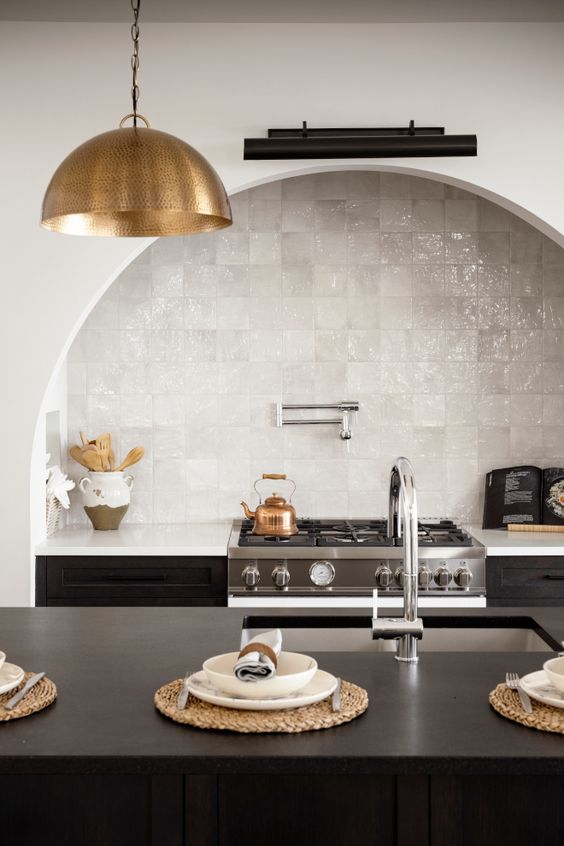 a chic kitchen with a black kitchen island and cabinets, an arched niche over the cooker with a built-in hood and white Zellige tiles
