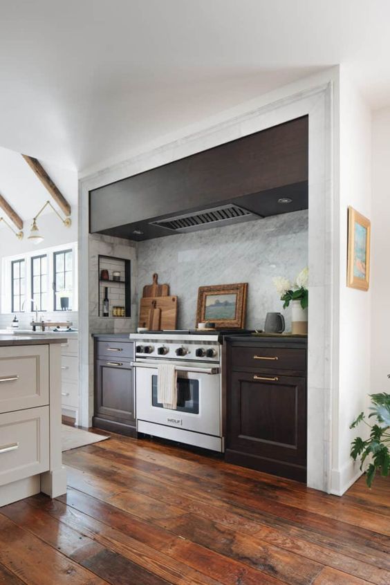 a modern farmhouse kitchen in white, with a large niche with dark-stained cabinets and a hood, some small shelves for condiments and oils