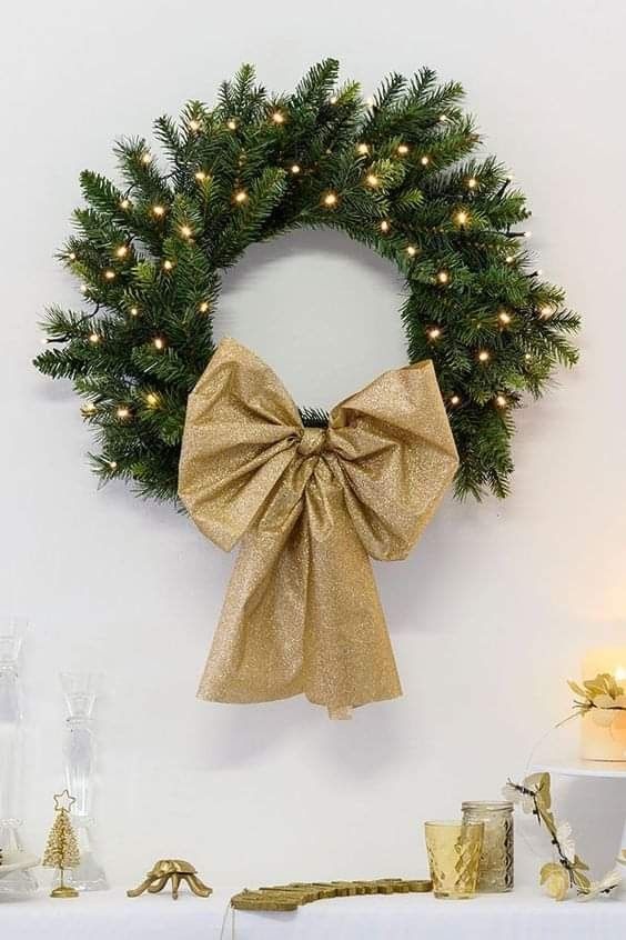 A glamorous evergreen Christmas wreath with lights and a gold glitter bow is a cool idea to implement