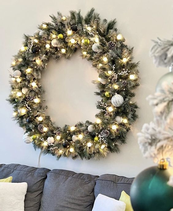 a large flocked Christmas wreath with black and white ornaments, snowy pine cones and lights
