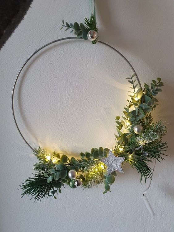 A minimalist Christmas wreath with greenery and evergreens, small ornaments and a silver star is wow