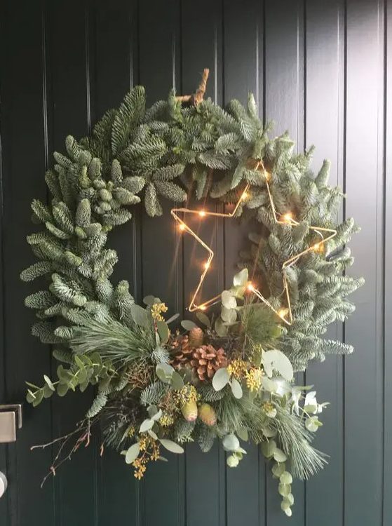 A modern Christmas wreath made with evergreens, branches, greenery, pine cones and a glowing star is a cool and memorable idea