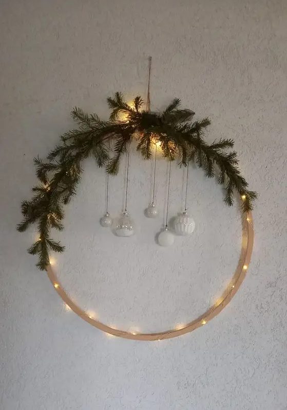 A modern Christmas wreath with lights, evergreens, and hanging white ornaments is a lovely idea for winter decor