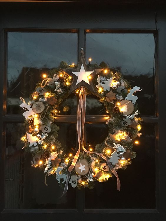 A Scandinavian Christmas wreath with evergreens, wooden slices, trees, deer, lights and stars is great for the holidays