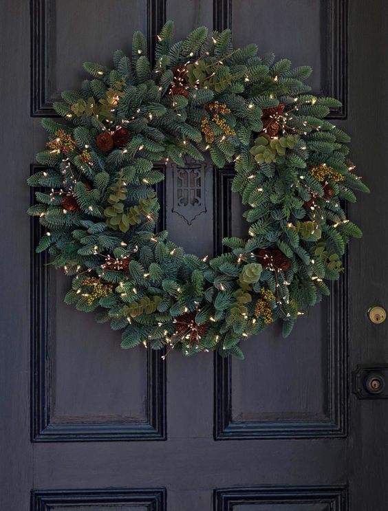 A stylish evergreen wreath with pine cones, berries and lights is a cozy idea for the holidays