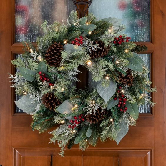 A textured Christmas wreath made of leaves and evergreens, pine cones and berries, and lights is beautiful