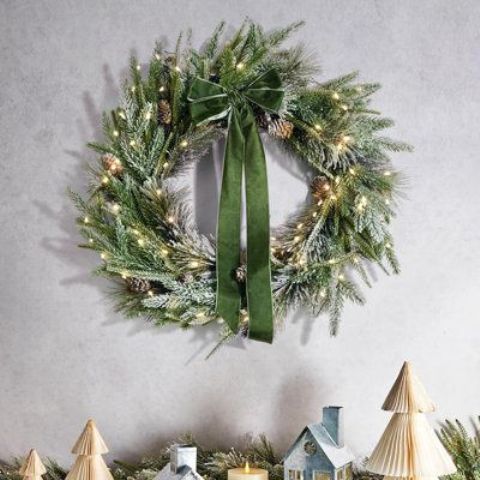 An evergreen Christmas wreath with pine cones and lights and a green bow is a glamorous and chic idea