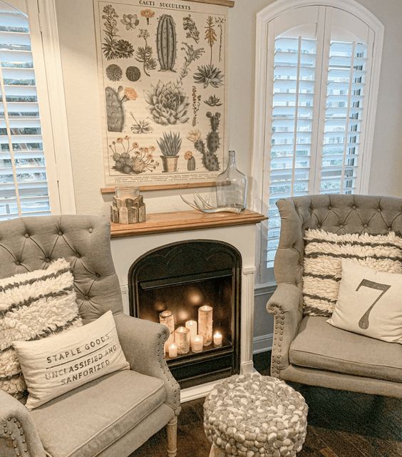 a built-in, non-working fireplace with pillar candles, gray chairs with cushions and a stool