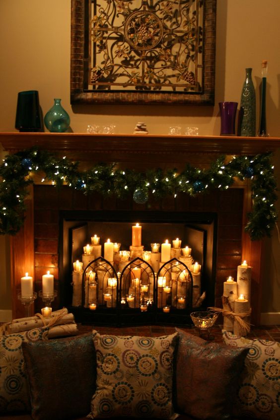 A Christmas fireplace with evergreen plants, lights, pillar candles inside and a beautiful screen is very cozy
