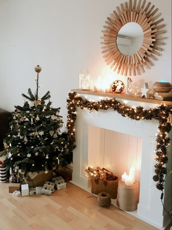 A faux fireplace with pine cones and lights, pillar candles, a pine cone and garland of lights, and candles on the mantel