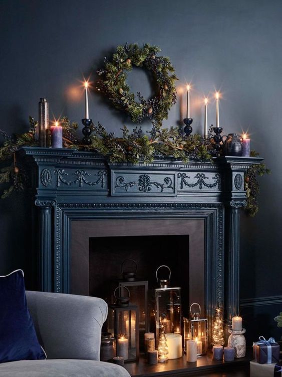 a beautiful dark fireplace with candle lanterns and candle holders, evergreen plants and candles on the mantel