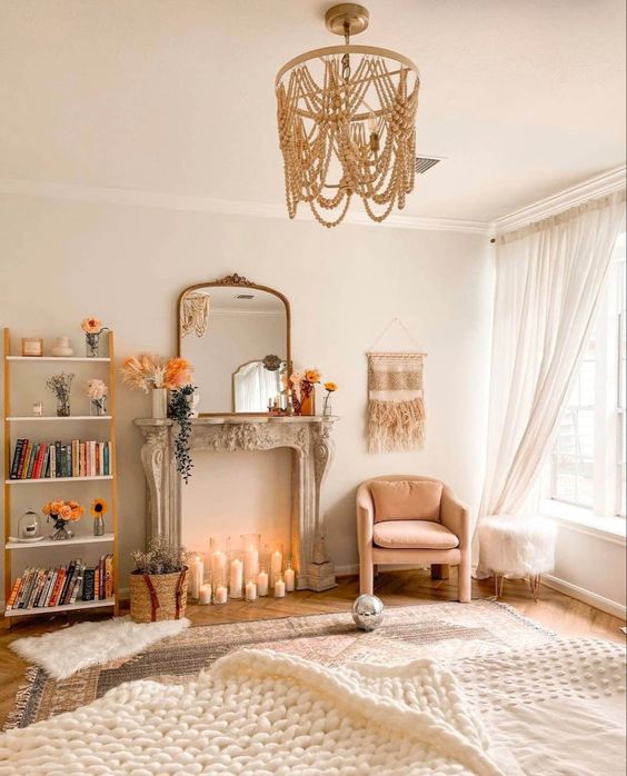 a neutral boho living room with a French fireplace and candles, a pink chair, a beaded chandelier and some rugs