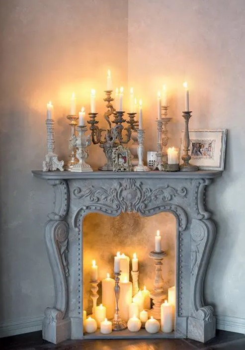 A sophisticated whitewashed vintage fireplace with candles of various sizes and shapes and vintage candle holders