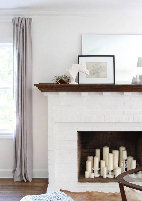 A white brick fireplace with pillar candles and some elegant decor on the mantel are super chic and cool
