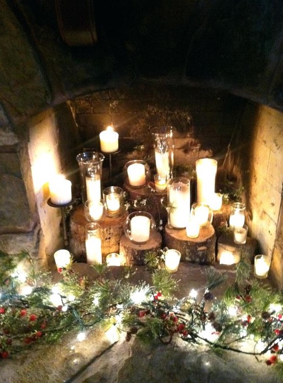 Tree stumps with candles in glass candle holders and some greenery and pine cones around them