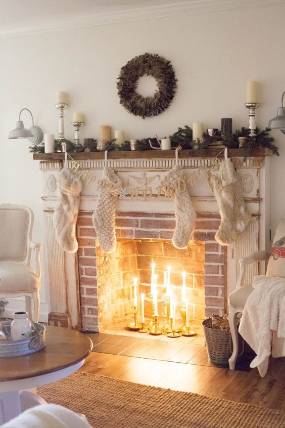 A brick fireplace with a white shabby chic mantel, with thin candles in candle holders in it and chic Christmas decorations