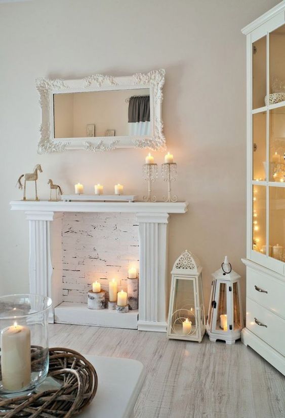 a faux white fireplace with candles on tree stumps, with candle lanterns and candles on the mantel