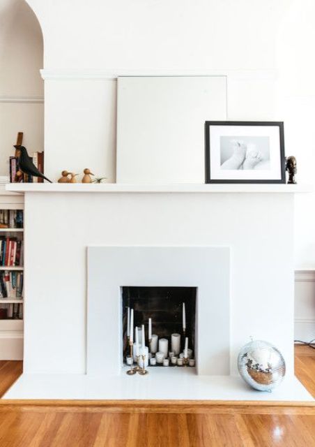 a neutral, minimalist artificial fireplace with many different candles inside and very laconic and minimalist decor on the mantel