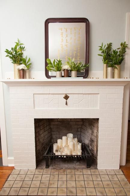 a non-functioning brick fireplace with a metal stand for firewood and pillar candles on top