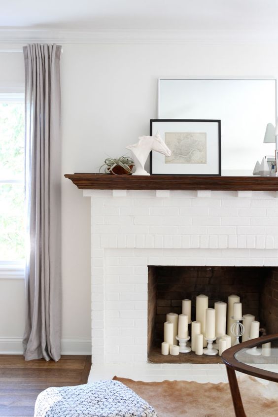 a white brick fireplace with pillar candles inside and a stained mantel with decor and plants