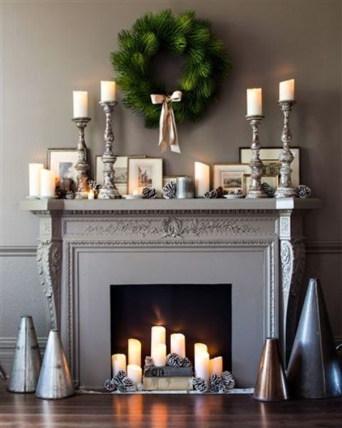 an elegant fireplace with a black screen, pillar candles, snowy pine cones and books and the same on the mantel