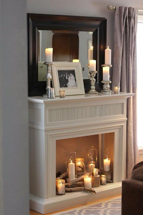 a simple, non-functioning fireplace with candles in various candle holders, tree stumps and wood, some candles on the mantel