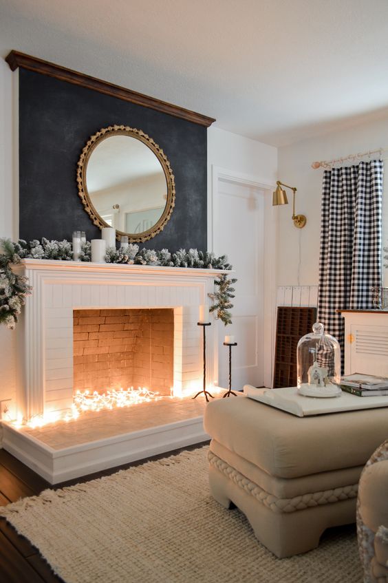 a non-working fireplace with lights inside, a snowy green garland and candles on the mantel
