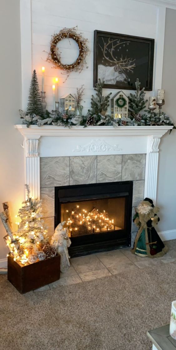 A winter fireplace with logs and lights inside, with a Christmas mantel and some branches