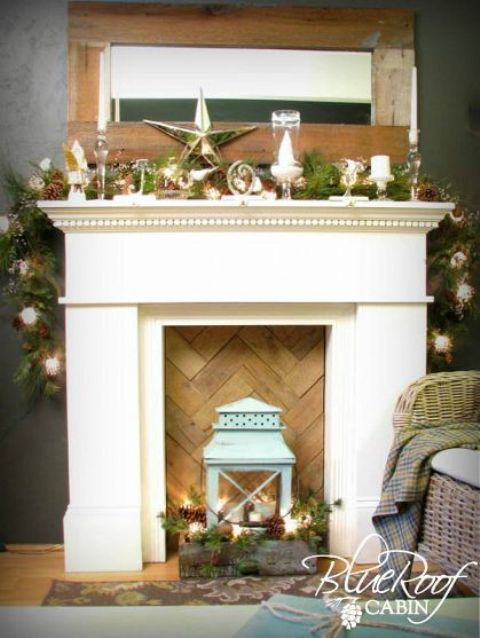a faux fireplace with a chevron wooden screen, a box with pine cones, candles, pine branches and a blue lantern
