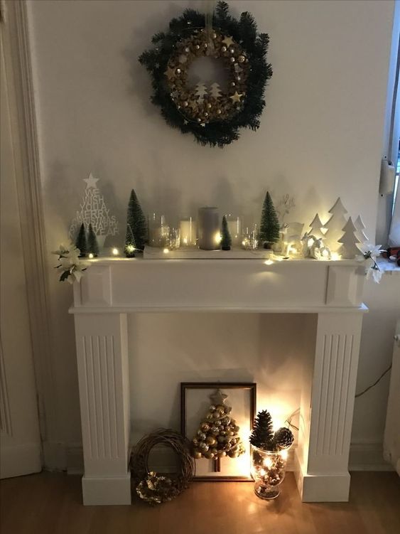 a faux fireplace with Christmas tree art, a vase of pine cones, a Christmas arrangement on the mantel