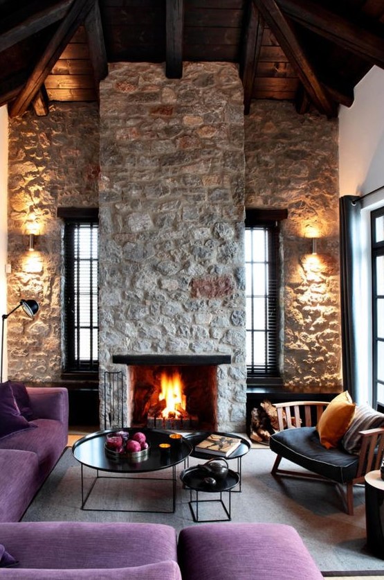 a bright, modern living room with rough stone walls and a fireplace, purple furniture and elegant round tables