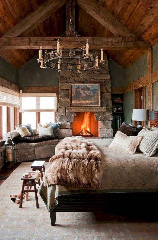 a cottage bedroom with a rough stone fireplace and bench, statement chandelier, wooden items and cozy bedding