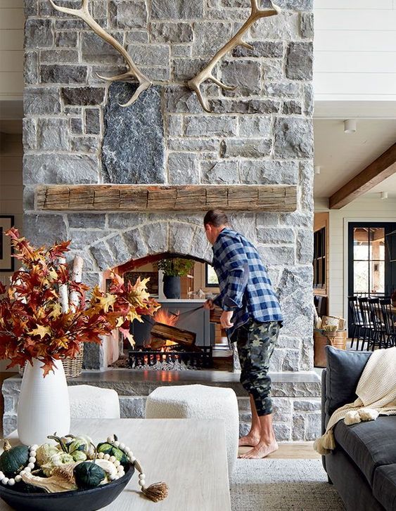 A chalet living room with a stone fireplace, coffee table and neutral stools, and pretty fall decor