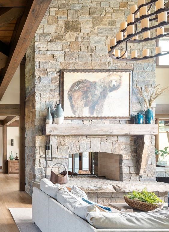 a chalet living room with a stone fireplace, a white sitting area, pretty decor and a beautiful tiered chandelier