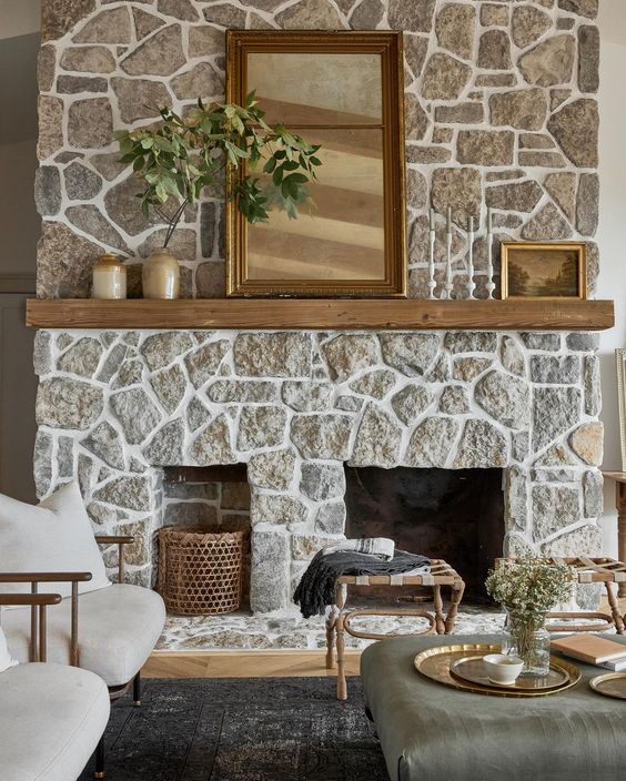 a chalet living room with a stone fireplace, neutral seating, an ottoman and a few stools, and natural decor