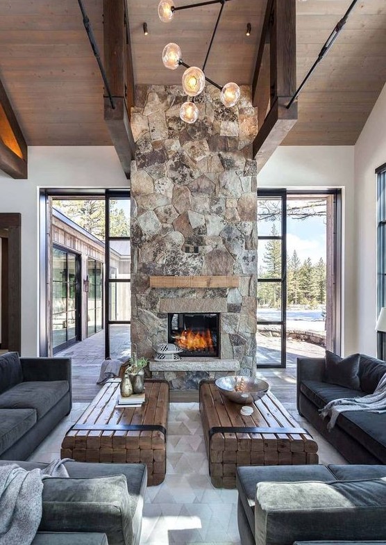 A chic, modern cabin space with dark furniture, wood slab tables and a spectacular stone fireplace with wood mantel