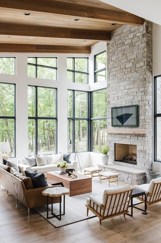 a clean and modern double height living room with a gray stone fireplace and wooden mantel as the centerpiece
