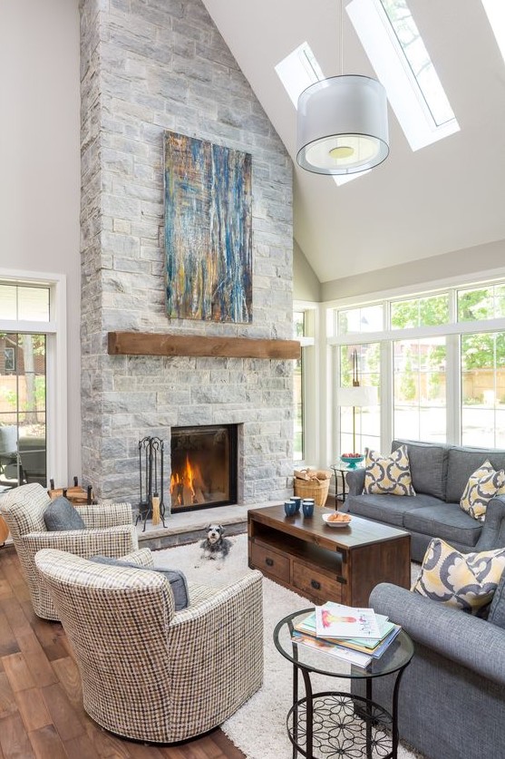 a clean, neutral double-height living room with a gray stone fireplace with wood-burning fireplace and bright blue artwork