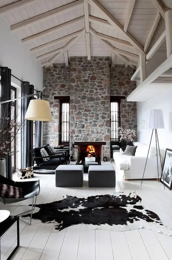 a modern living room with white walls, a whitewashed wooden ceiling, a stone-clad fireplace and cool furniture