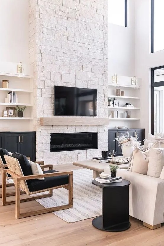 a contrasting living room with a stone fireplace, shelves and built-in cupboards, a white sofa, black chairs and a black side table