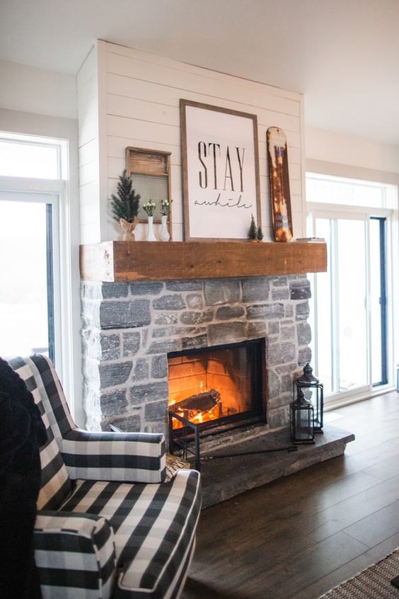 A farmhouse living room with a stone fireplace, a mantel with winter decor, and a checkered chair feels and looks very cozy