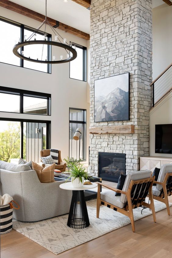 a farmhouse living room with a stone fireplace, neutral seating, chairs, coffee tables and a chandelier