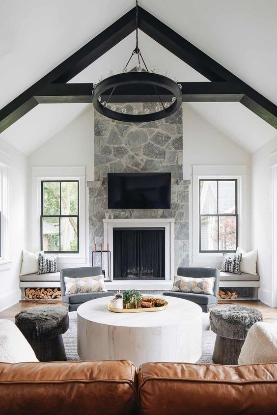 a farmhouse living room with a stone fireplace, window sills and storage, an amber sofa and neutral ottomans