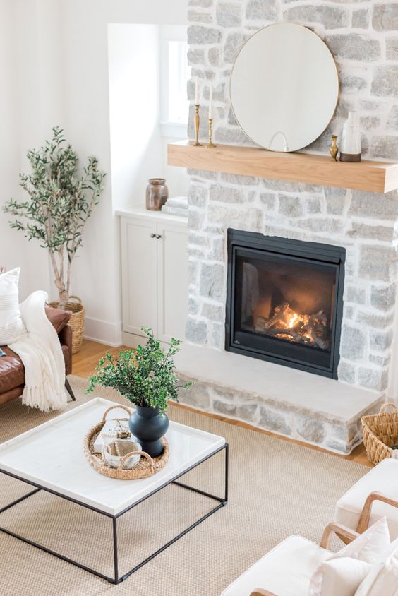 a stone-clad fireplace with mantel, a leather sofa, a coffee table and neutral chairs, potted plants