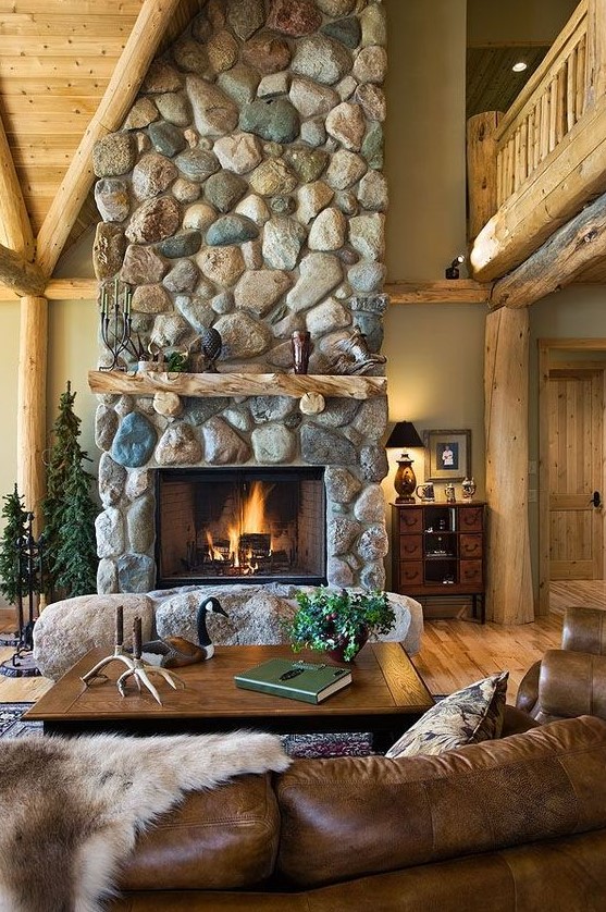 A beautiful cabin room with a large stone fireplace with stones at the base and leather and wood furniture