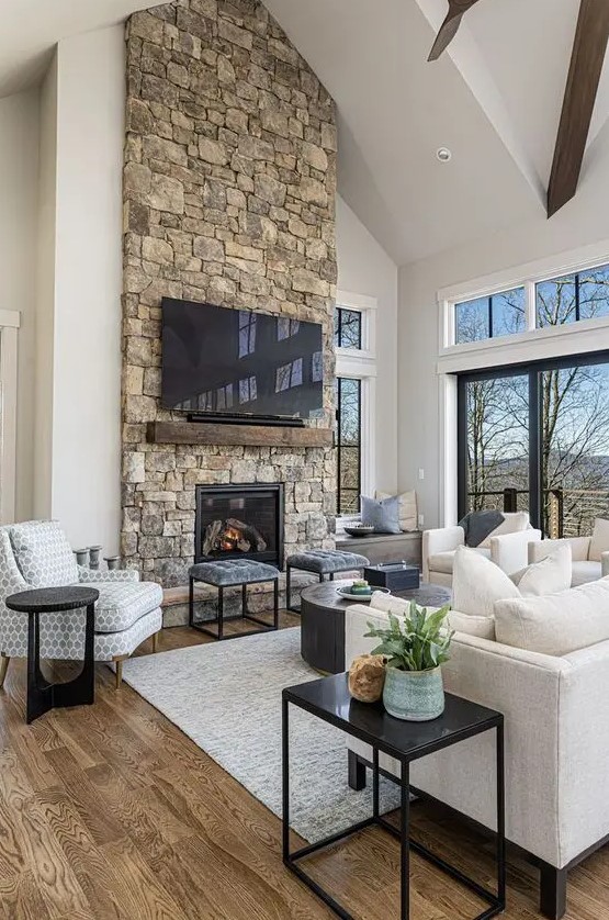 a modern chalet living room with a stone fireplace, neutral seating, a coffee table and stools