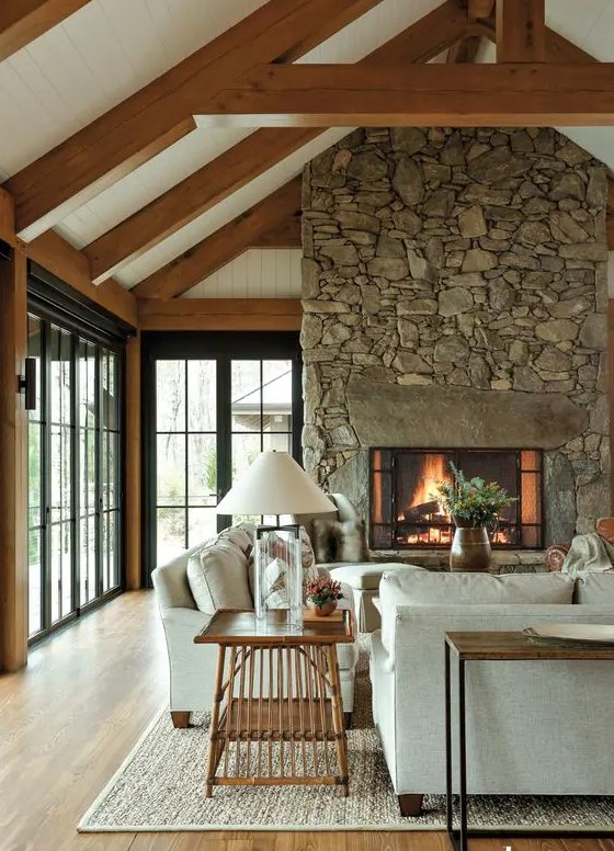 a modern chalet living room with a stone fireplace, neutral seating, a stained side table and a console