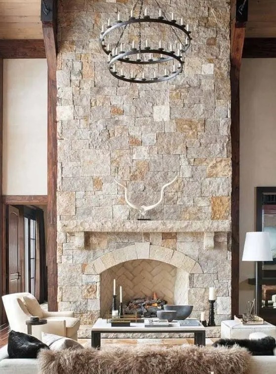 a modern chalet living room with a stone fireplace, neutral seating and a tiered metal chandelier