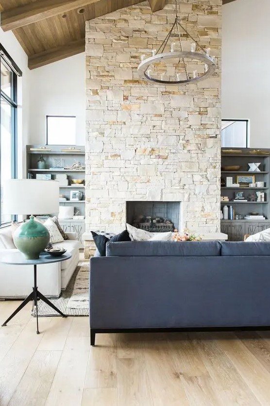 A modern farmhouse living room with a navy blue sofa, a white sofa, a coffee table, a stone fireplace and a chandelier