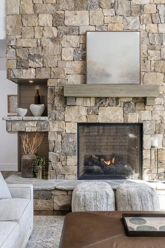 a modern living room with a stone fireplace and mantel, some alcove shelves and seating, and a leather stool